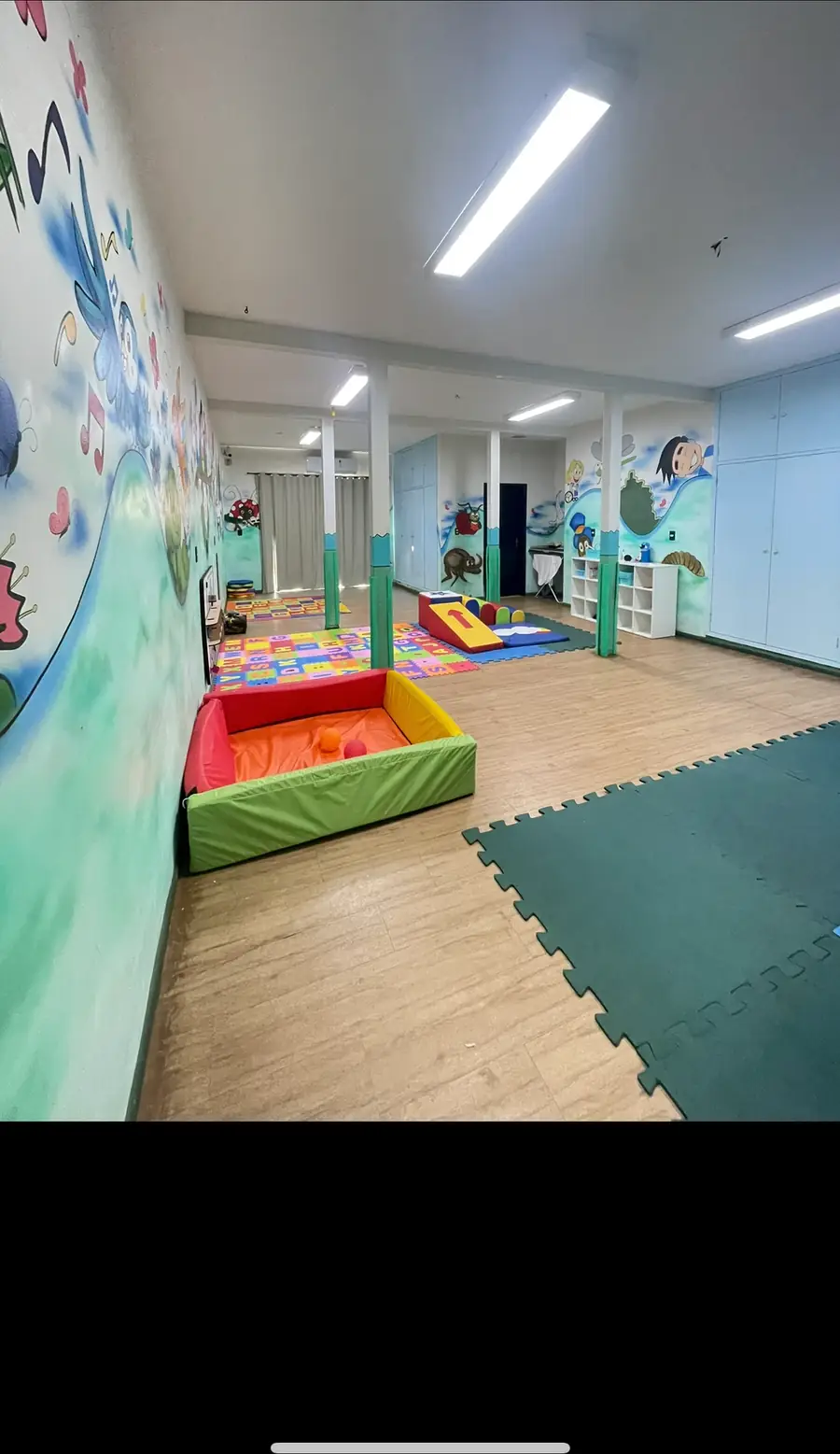 Sala interna com piso de tatame, mural pintado na parede e piscina de bolinhas